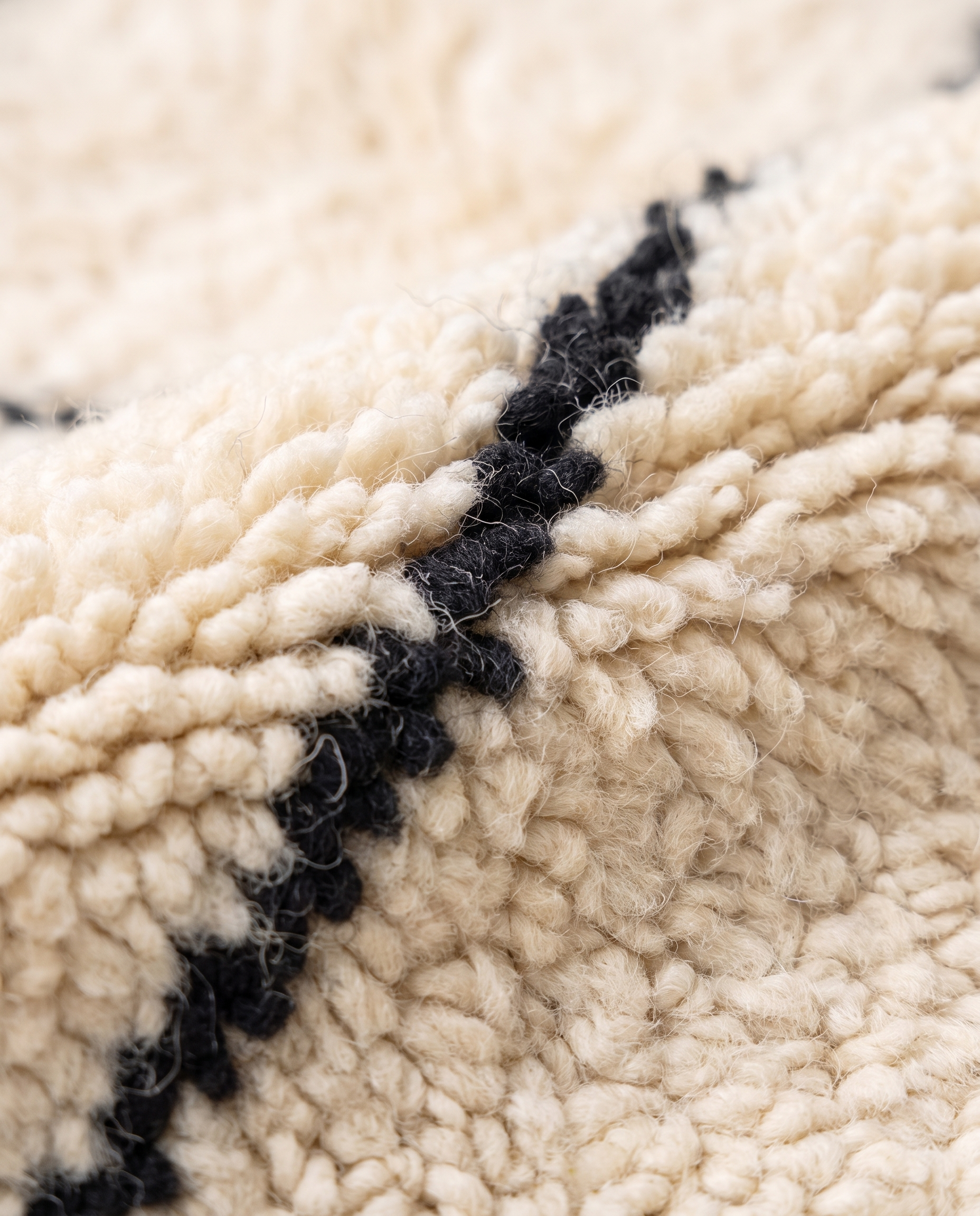 Close-up of hand-knotted ivory wool pile with black diamond line — Beni Ourain rug texture