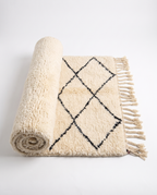 Half-rolled Beni Ourain rug showing thick ivory wool pile on white studio background