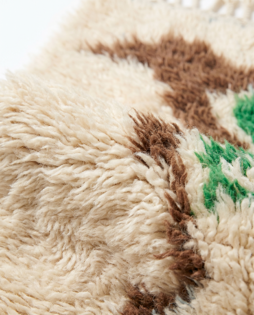 Close-up of plush cream Mrirt wool pile with brown abstract motif — texture detail on white studio background