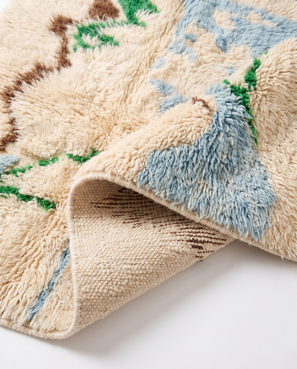 Folded corner of Mrirt rug showing dense wool pile and handwoven back — white studio background