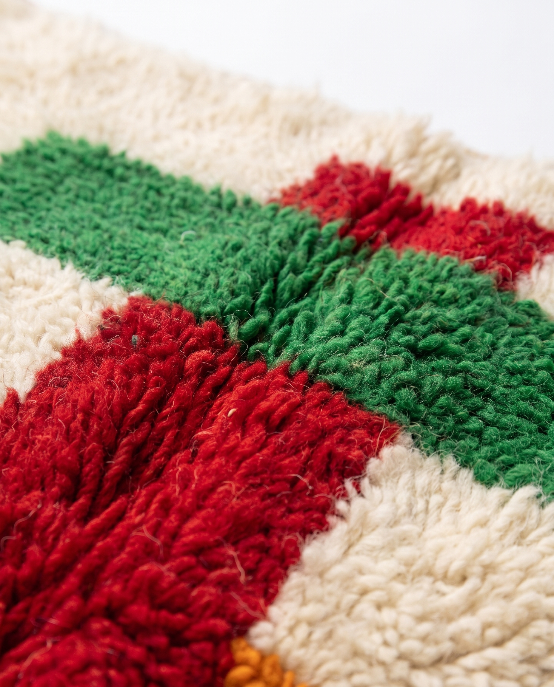 Close-up of wool pile where red stripe meets green crossbar — colorful runner rug texture on white studio background