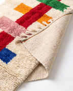 Folded corner of colorful runner rug showing wool pile and handwoven back on white studio background