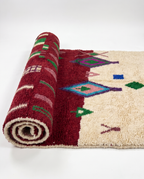 Burgundy and ivory Boujaad rug half-rolled on white studio background