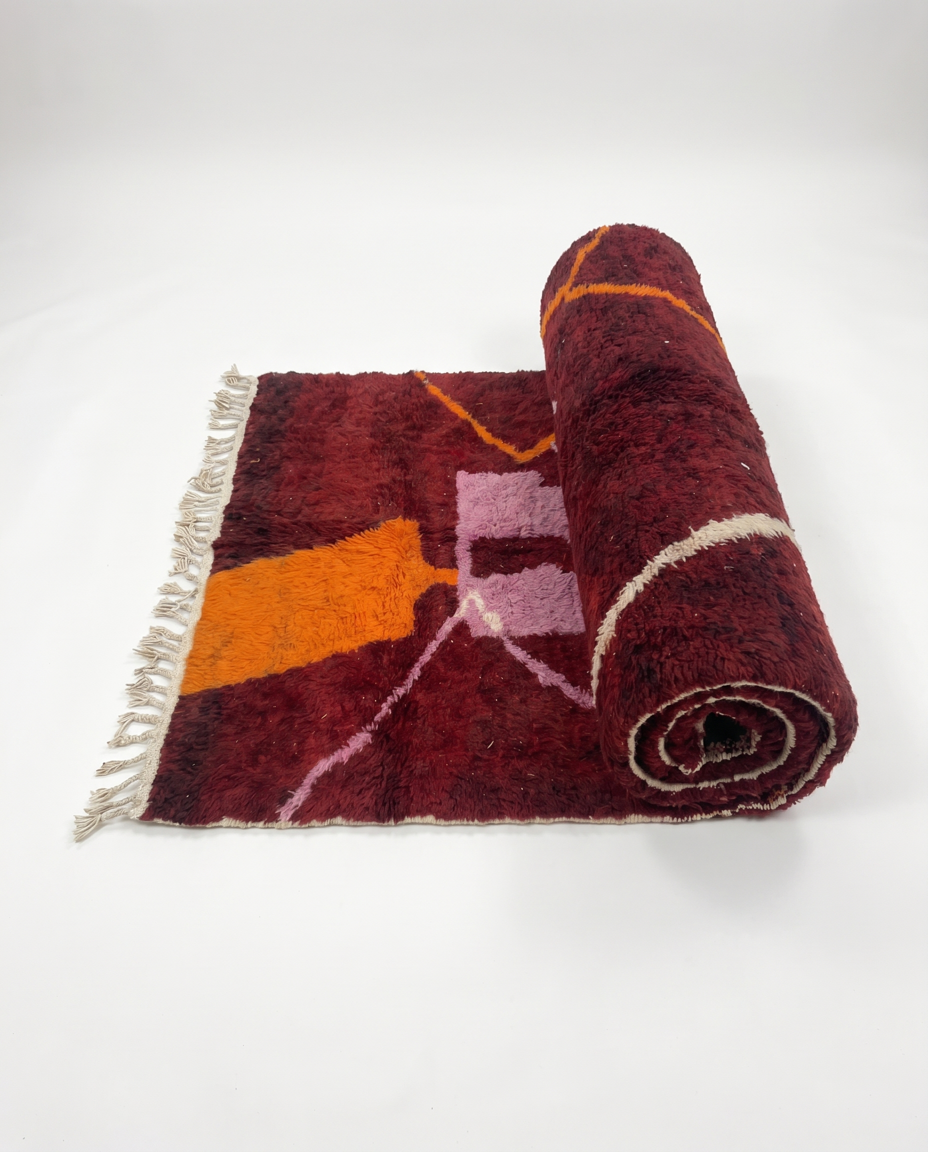 Wine red Boujaad rug half-rolled on white studio background