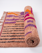 Blush terracotta Boujaad rug half-rolled on white studio background