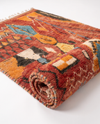 Rust and amber Boujaad rug half-rolled on white studio background
