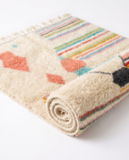 Pastel rainbow Azilal rug half-rolled on white studio background